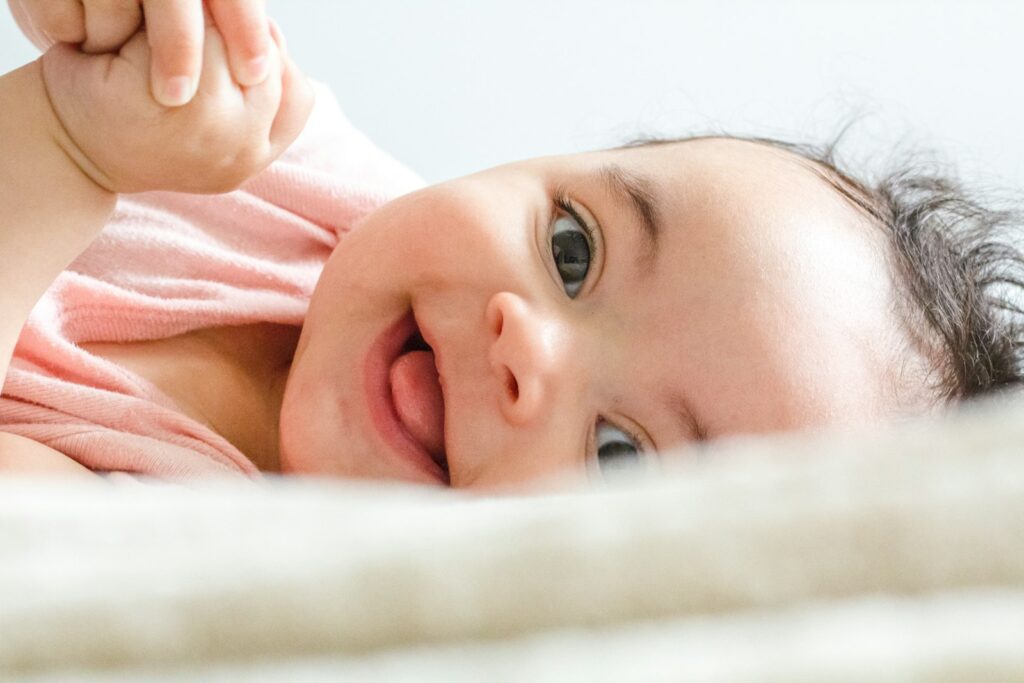 Lächelndes Baby auf weißer Decke – nach den Impfungen beim Baby helfen Nähe und Ruhe